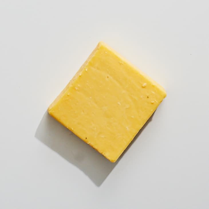 An overhead photo of aged cheddar cheese on a white surface.