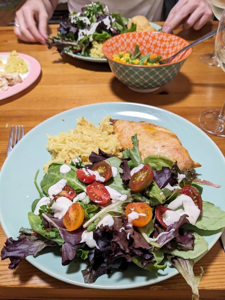 blue plate with mixed green salad, cherry tomatoes, dressing, and bread