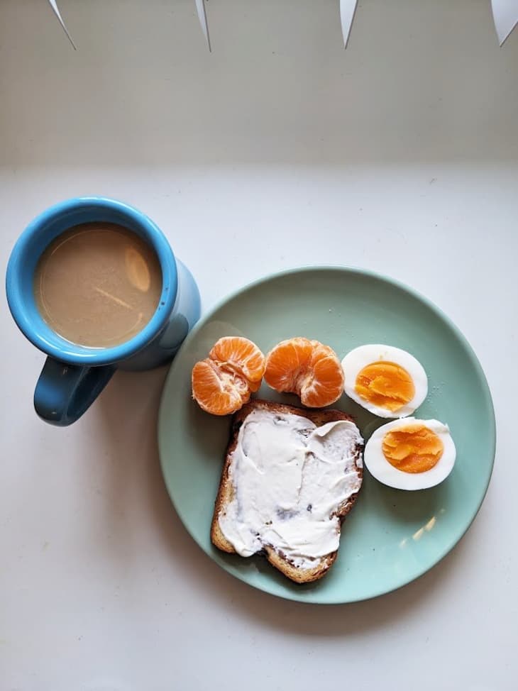 hard boiled egg, toast with cream cheese, an orange and a cup of coffee