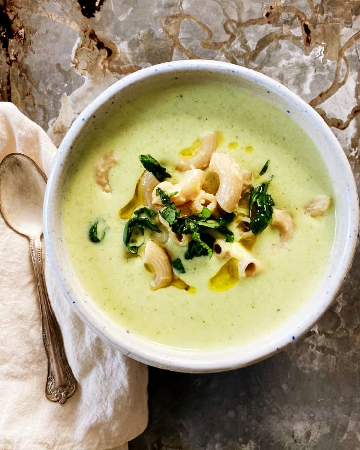 creamy broccoli soup sits in a white bowl with noodles peeking through the surface