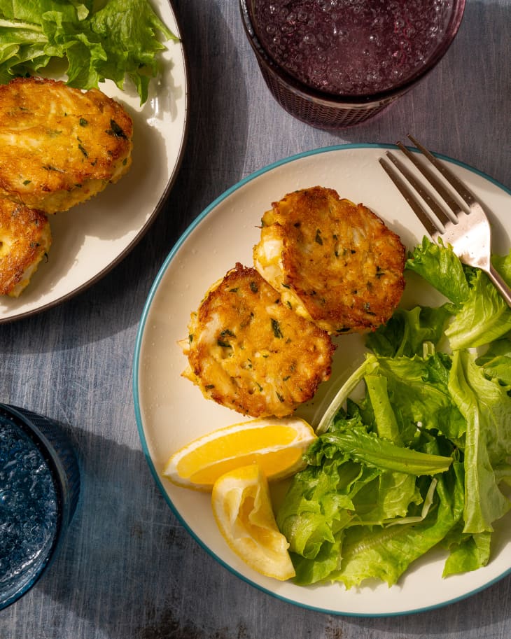 crab cakes on plate with greens, lemons, and a fork