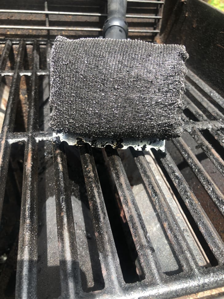 Grill brush cleaning a barbecue grate with visible metal bristles.