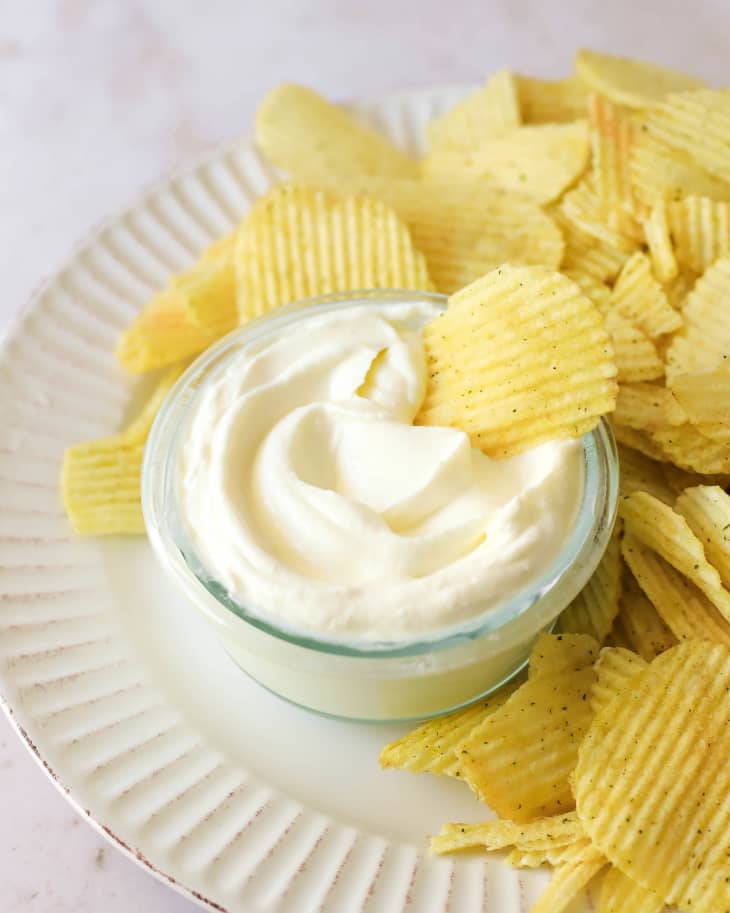 White plate with ruffled potato chips and glass bowl of sour cream.
