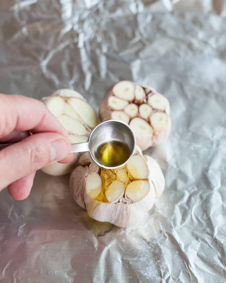 a tablespoon of oil being poured onto a head of raw garlic