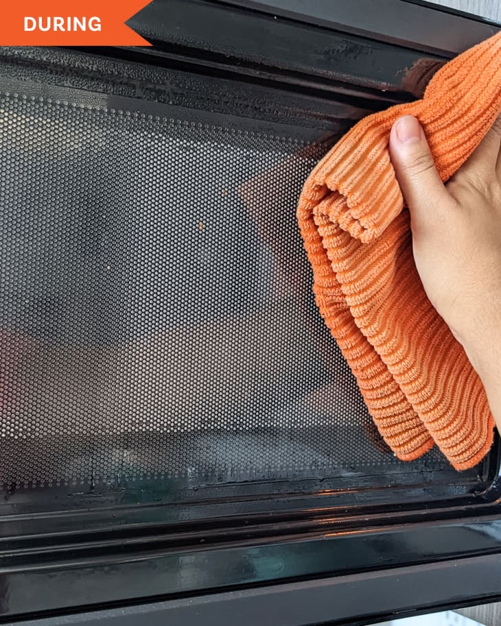 Hand using microfiber cloth to clean inside of microwave.