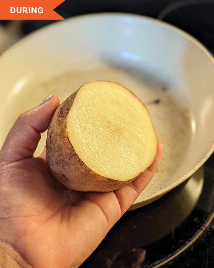 Someone holding cut potato to clean skillet