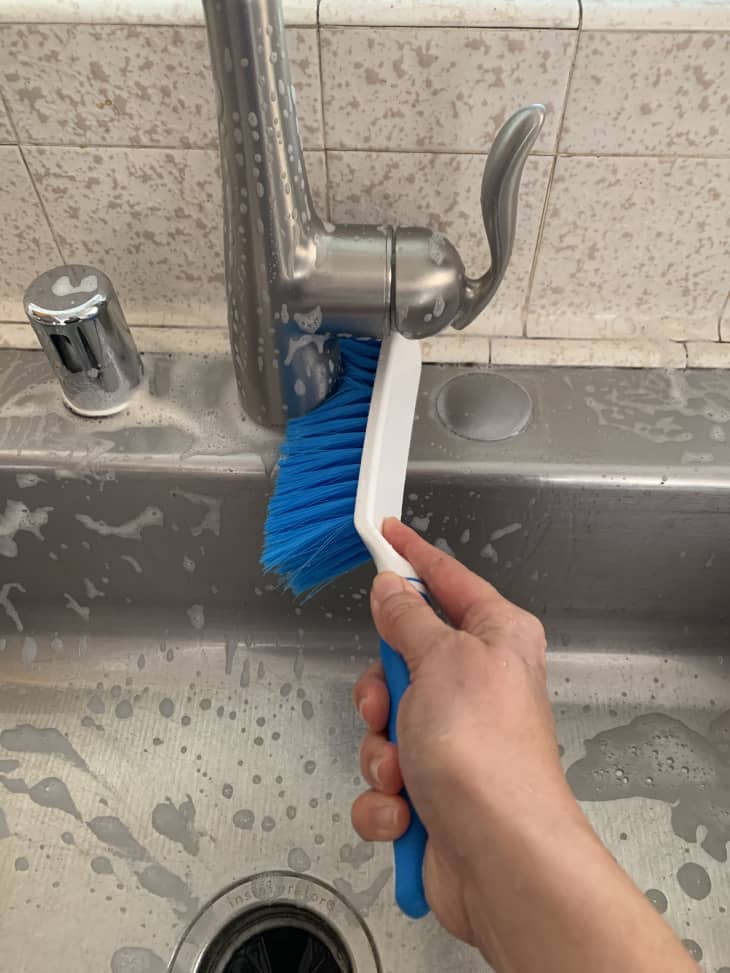 scrubbing the bottom of the sink faucet with a brush