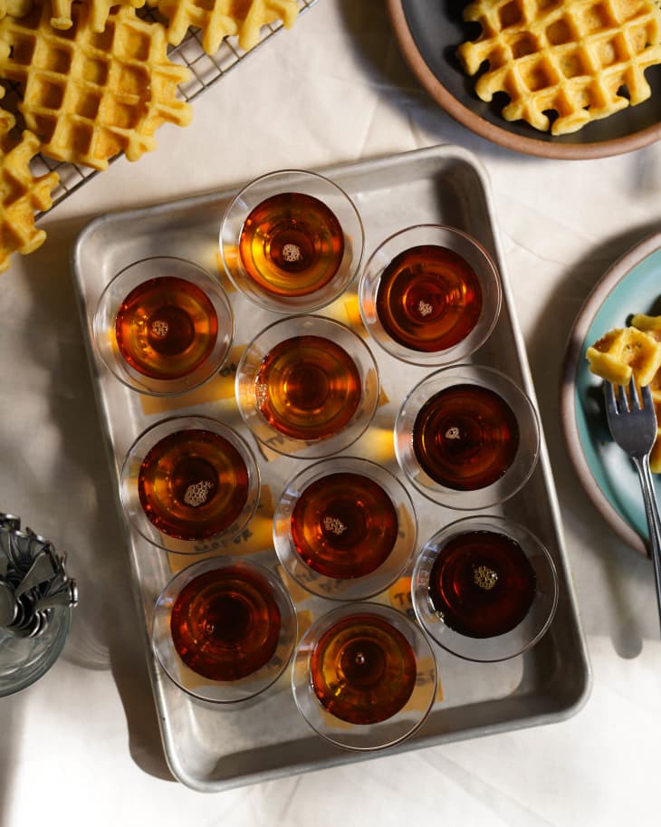 10 small containers of maple syrup on a sheet pan surrounded by waffles