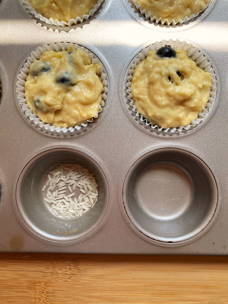 muffin batter in lined tin, one empty hole filled with grains of rice