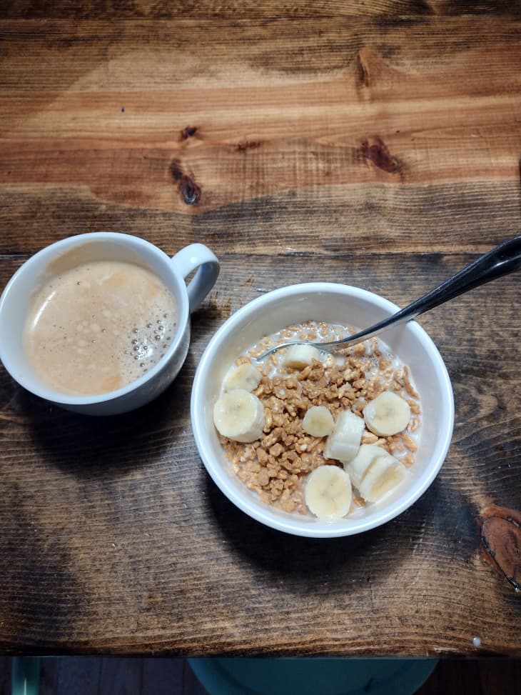 Granola with bananas in bowl with mug of coffee