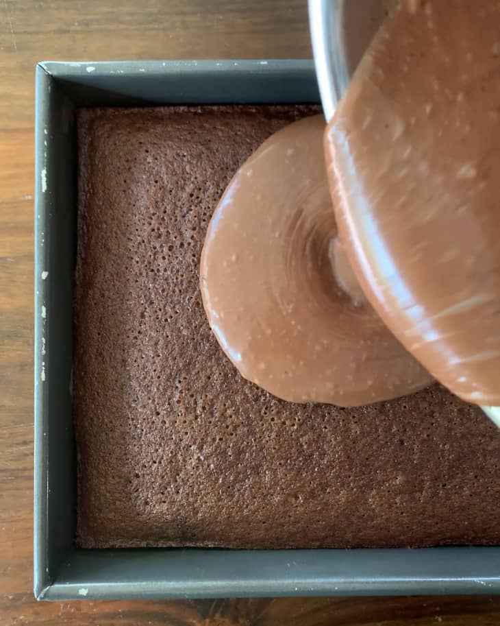 Coke cake in cake pan, baked, someone pouring frosting on top from a bowl