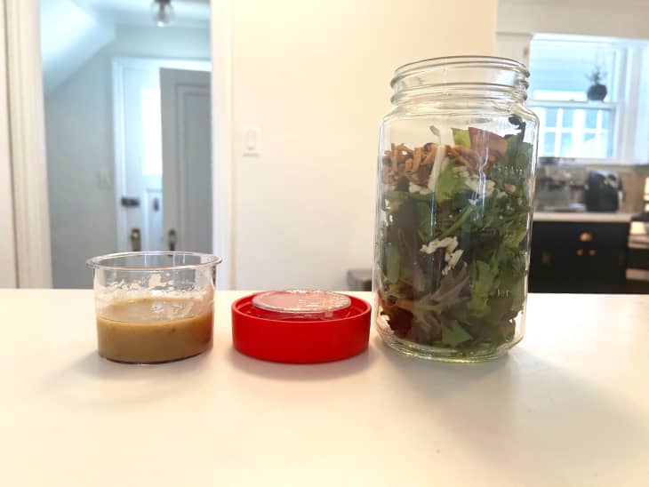 Salad in Pyrex storage container with salad dressing beside on counter.
