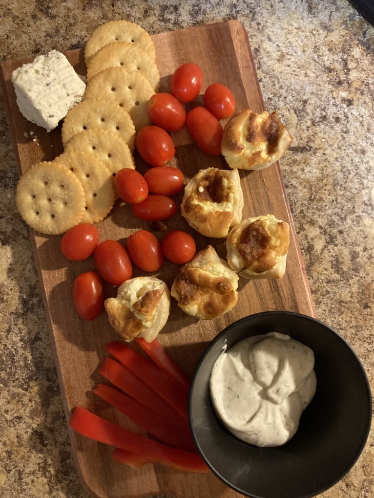 snack board with crackers, tomatoes, cheese, and dip