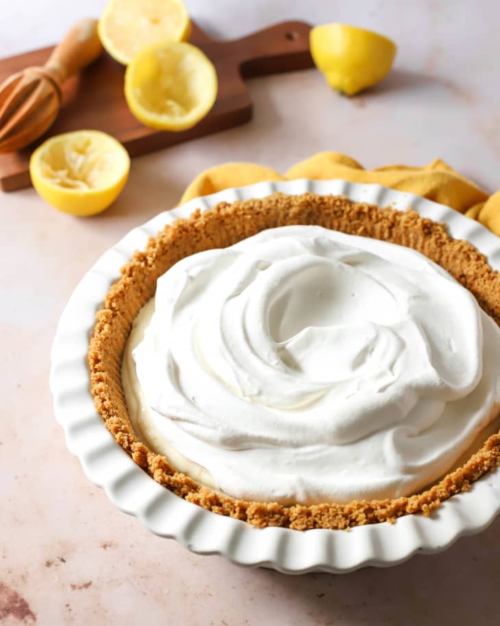 Whole lemon icebox cake in pie dish with halved lemons in background.