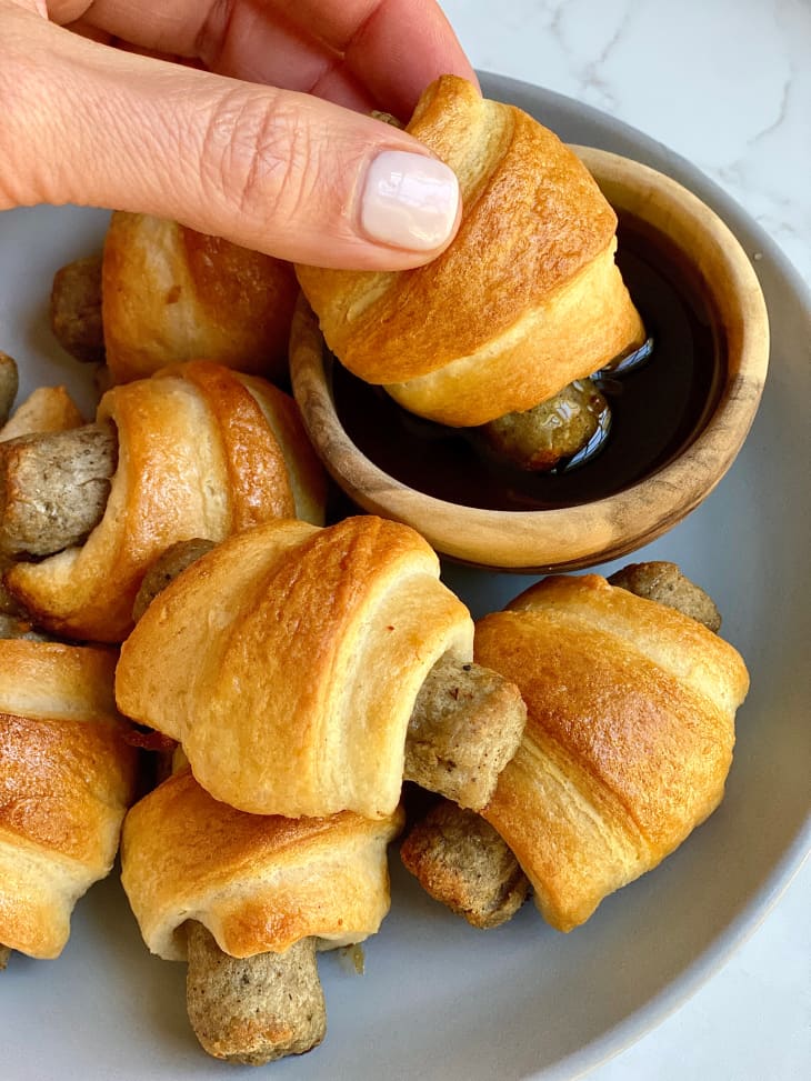 Someone dipping pigs in a blanket into syrup.