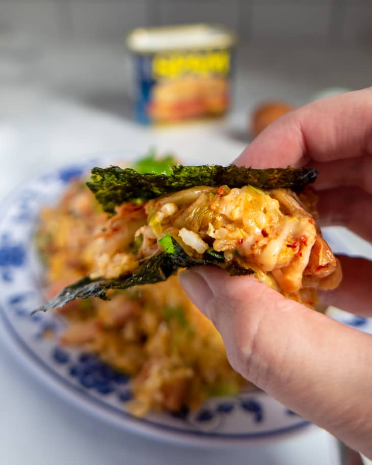 Someone holding seaweed wrapped in cheesy egg rice with spam and kimchi.