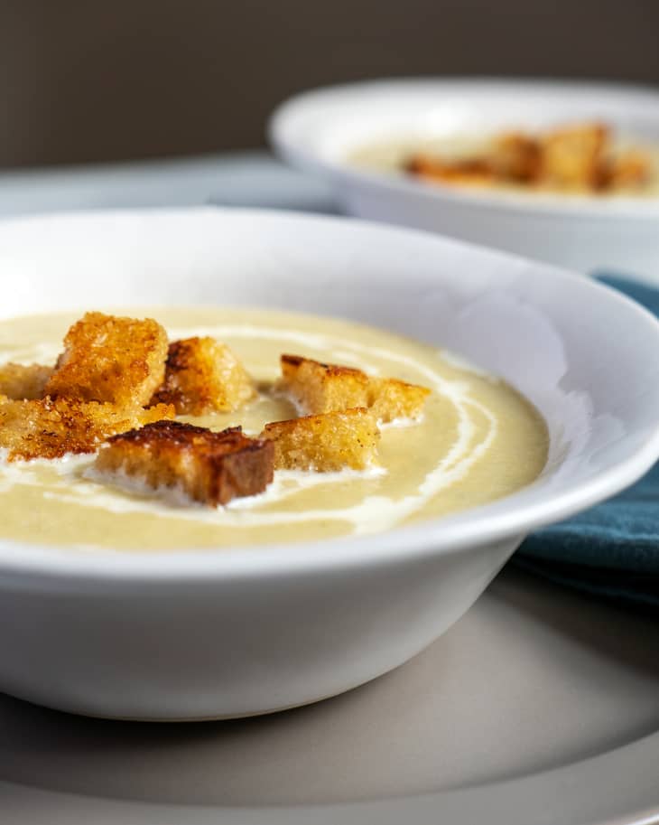 Cream of Artichoke Soup in bowl with croutons and lemons. Blue cloth napkin, lemon wedges, and spoon