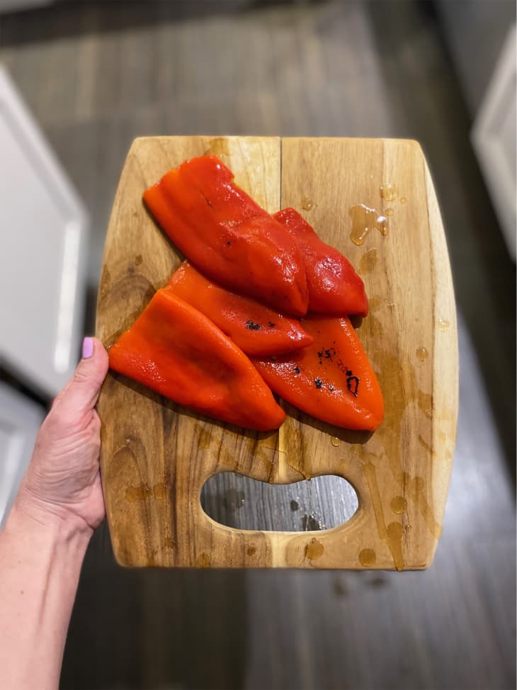 Someone holding cutting board with Divina roasted red pepper on top.
