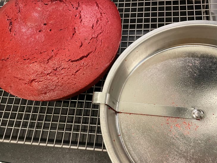 Red velvet cake on cooling rack beside easy release cake pan.