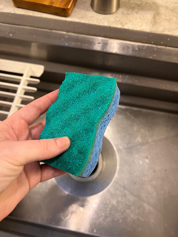 Someone holding sponge above the sink.