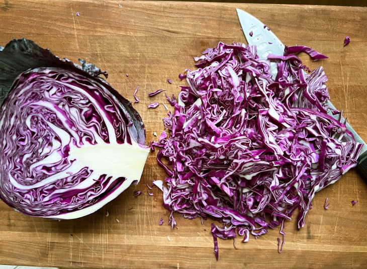 Halved cabbage on cutting board with one half shredded.