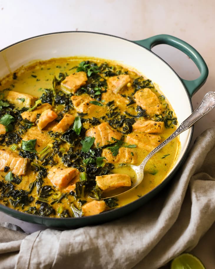 Kale and coconut salmon curry in dutch oven with serving spoon inside.