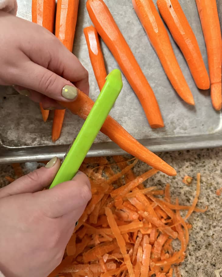 hands shown peeling carrots with Dreamfarm Sharple peeler over cutting board