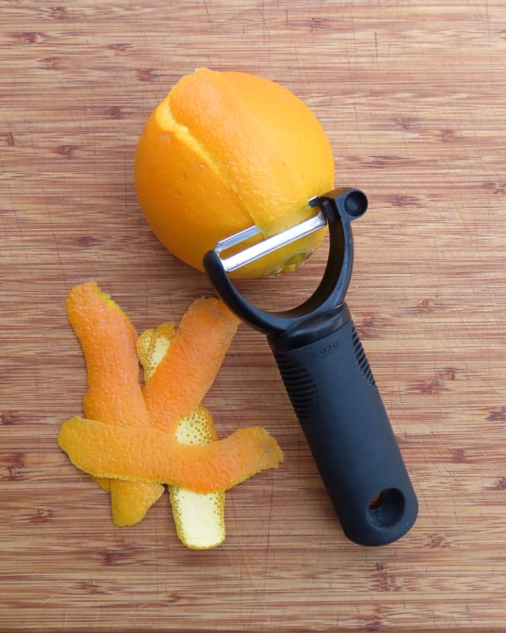 Overhead photo of someone peeling an orange with the OXO good grips y peeler on cutting board