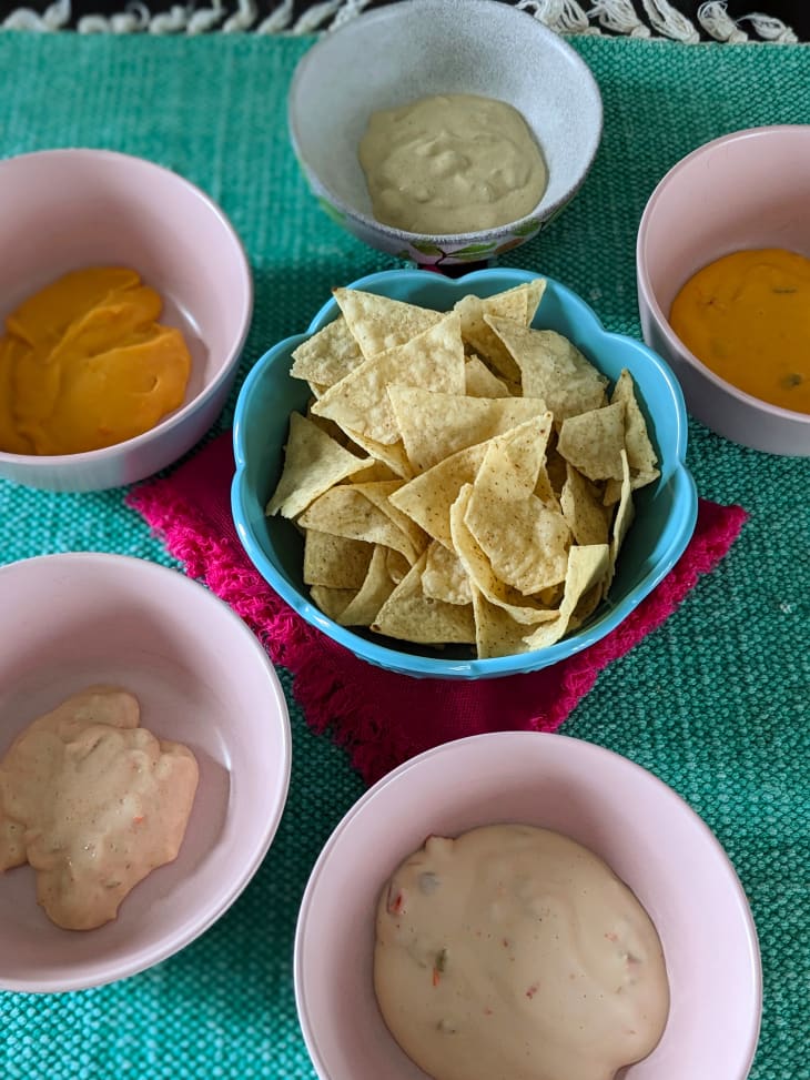 Various queso dips in bowls surrounding a bowl of tortilla.