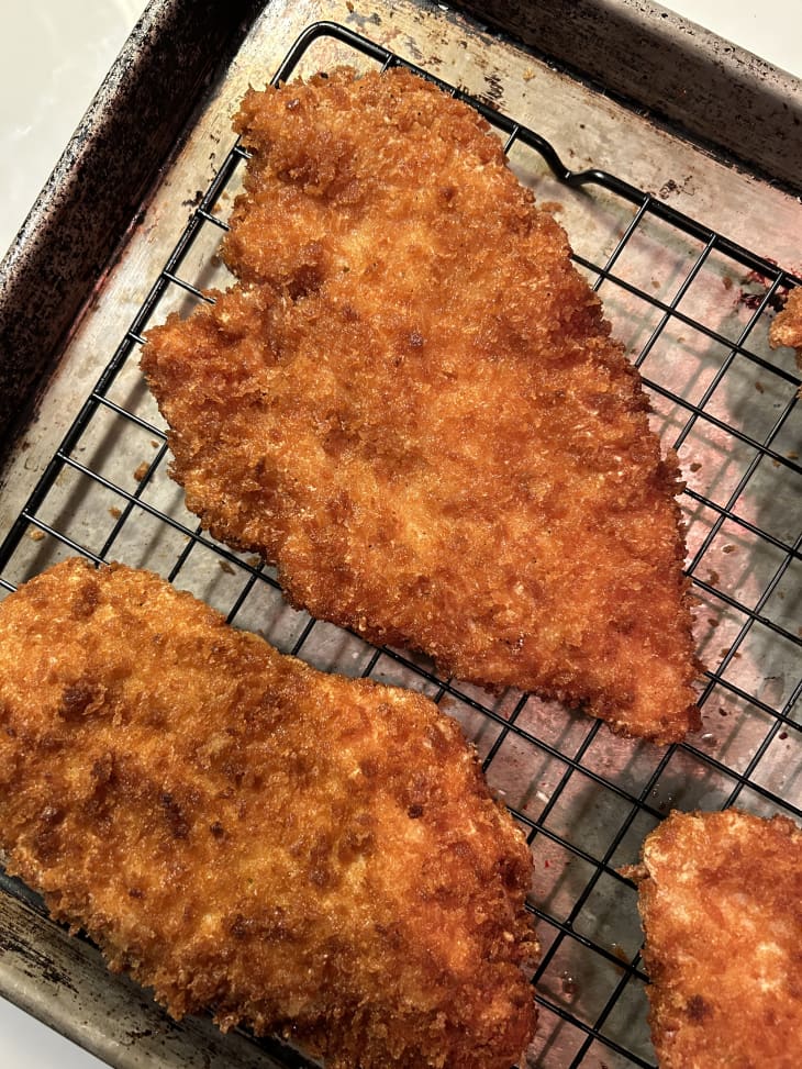 Breaded chicken cutlets cooling on rack over sheet pan