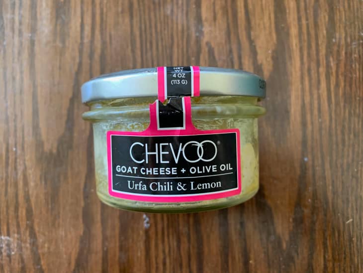 Jar of Chevoo goat cheese with urfa chili and lemon on wooden surface.