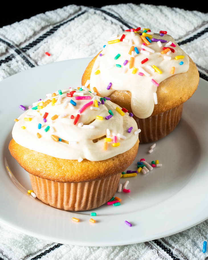 2 vanilla cupcakes on plate with frosting and sprinkles.