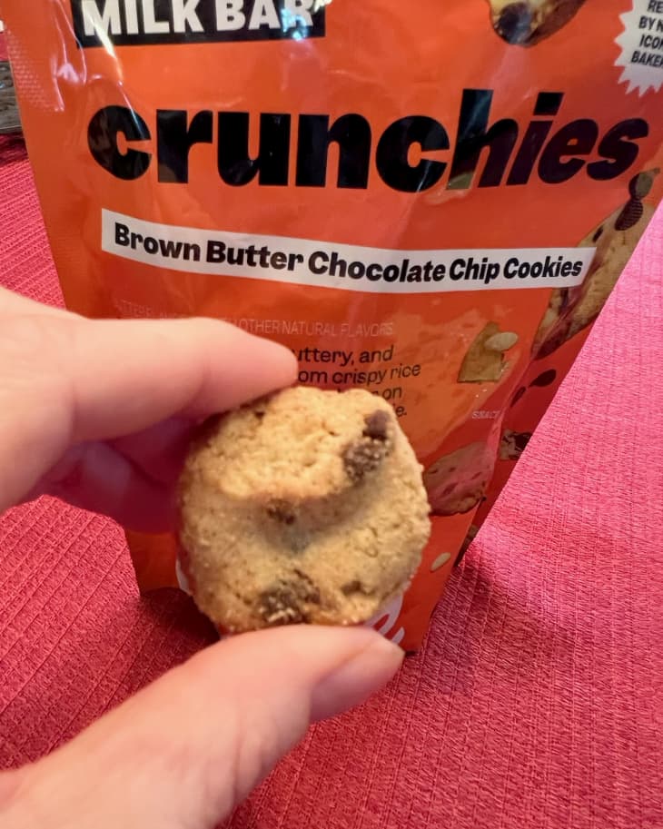 Milk Bar Crunchies cookies. Bag in the background and someone holding up a cookie in front