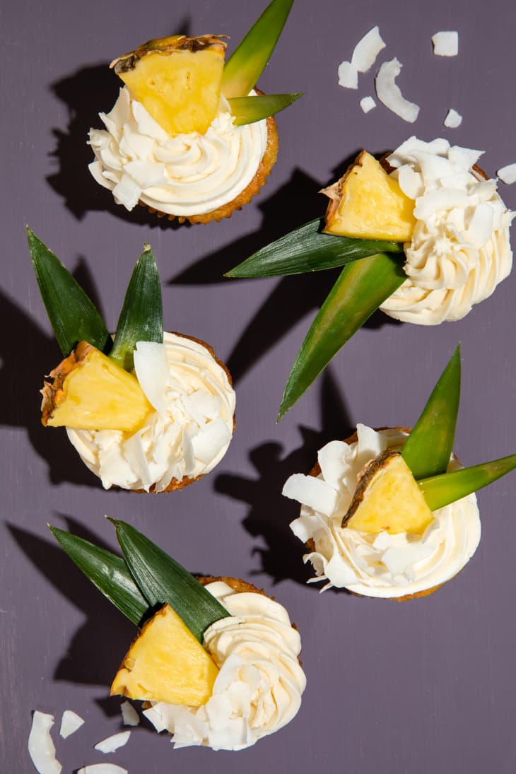 Top view of pina colada cupcakes with pineapple wedge garnishes on purple background.