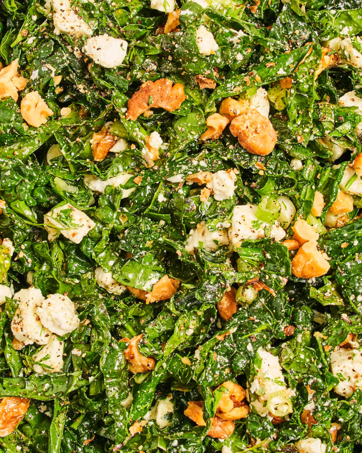 Overhead photo of Spanakopita Kale Salad with ingredients around (pitas on plate, feta cheese, basil, walnuts)