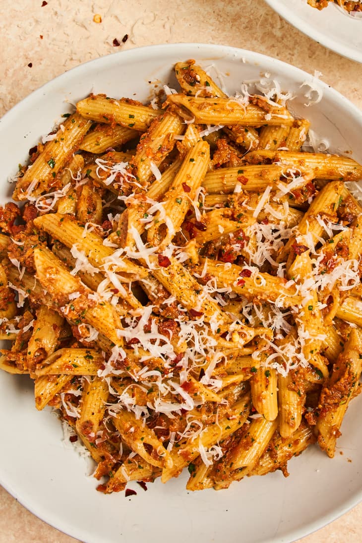 Pasta with sun-dried tomato pesto topped with cheese and red pepper flakes in a bowl.