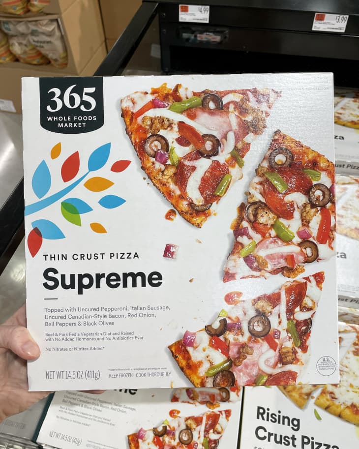 Someone holding up frozen Whole Foods 365 This Crust Supreme Pizza in store
