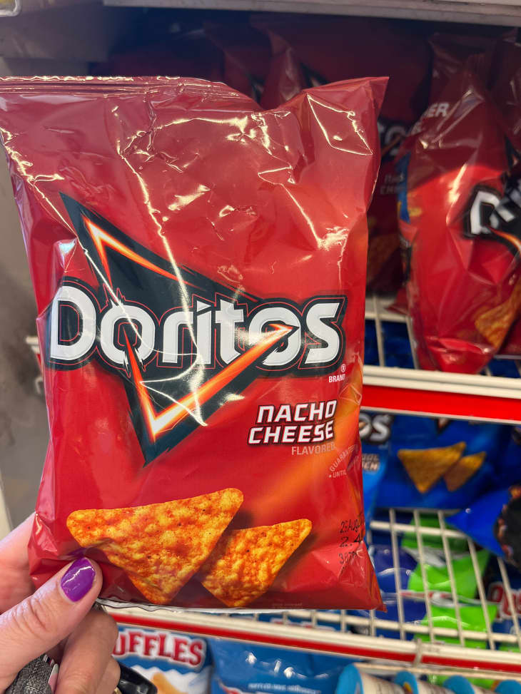 Someone holding bag of  Nacho Cheese Doritos in gas station.