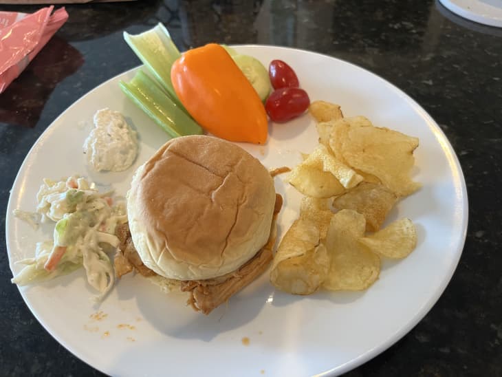 bbq chicken sandwich in bun with coleslaw, raw vegetables, potato chips