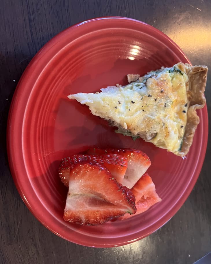 a slice of quiche and some strawberries on red plate