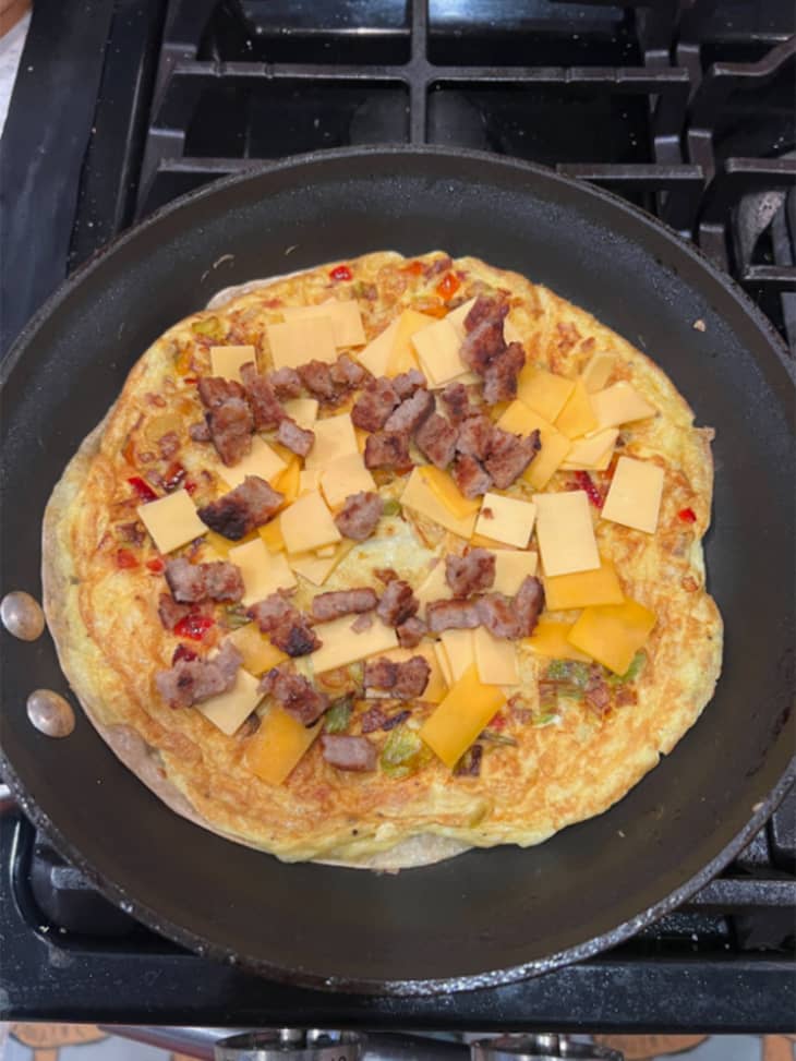 Eggs, meats, and cheeses cooking in a quesadilla on a black pan