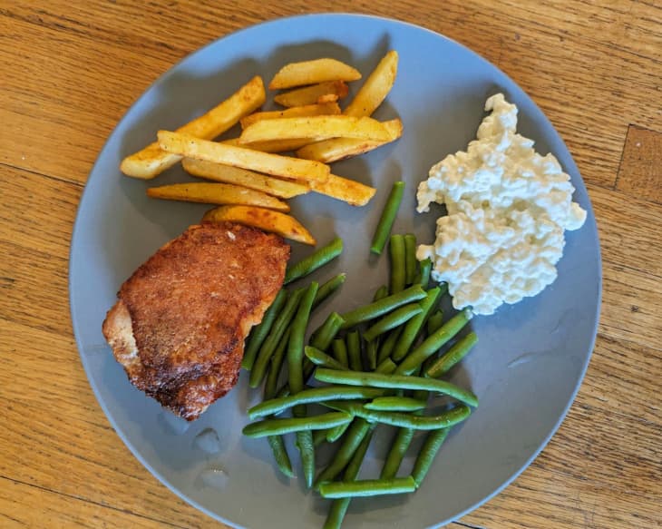 piece of meat, french fires, green beans, cottage cheese, blue plate, wood table