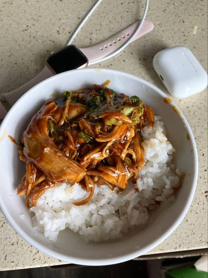 Bowl of rice with saucy meat and broccoli on countertop.