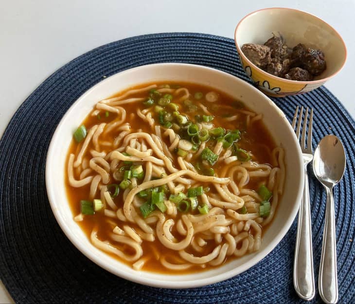 Bowl of noodles in broth with meatballs on the side.