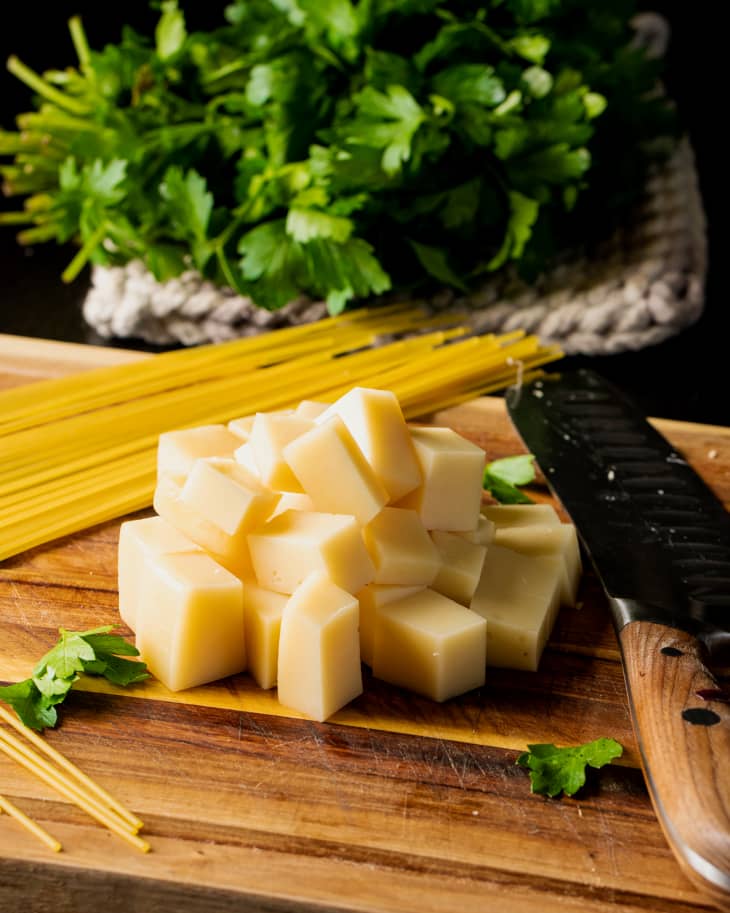 Cheese cut into cubes with noodles and fresh herbs surrounding to make french onion soup noodles.