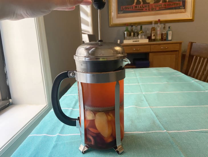 Someone pressing fruit in a french press to make an Aperol spritz sangria