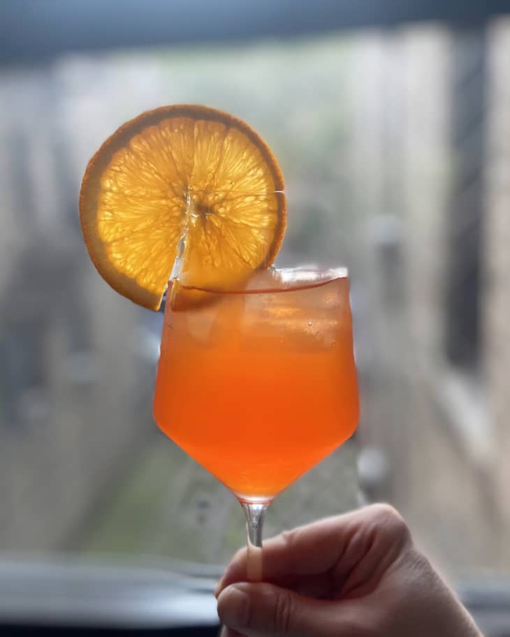 Someone holding up a wine glass with Aperol spritz sangria garnished with an orange slice