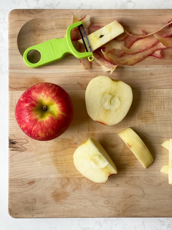 An apple being peeled on a wooden cutting board
