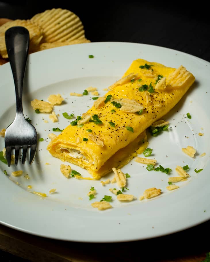 Slice out of French omelet on plate garnished with potato chips and parsley. Fork on the side.