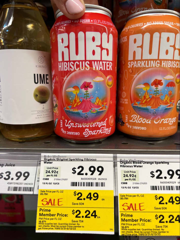 Someone holding can of Ruby Hibiscus Water in grocery store refrigerator.